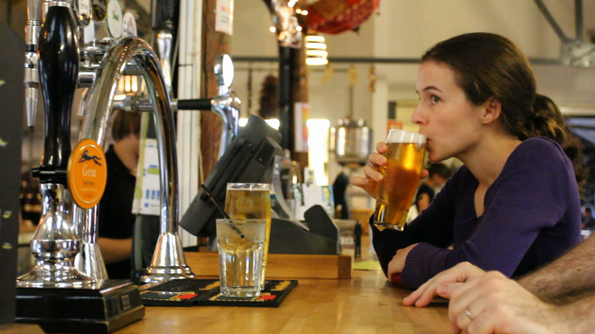 Young woman drinking lager out of a pint glass at the bar in Bocabar